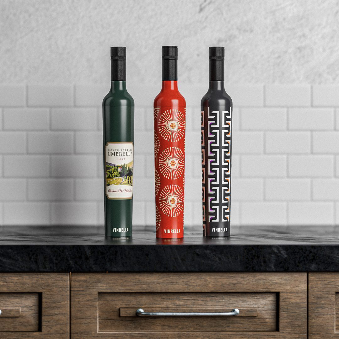 Three tall, slender wine bottles with different colorful labels standing on a black marble countertop against a white subway tile backsplash.