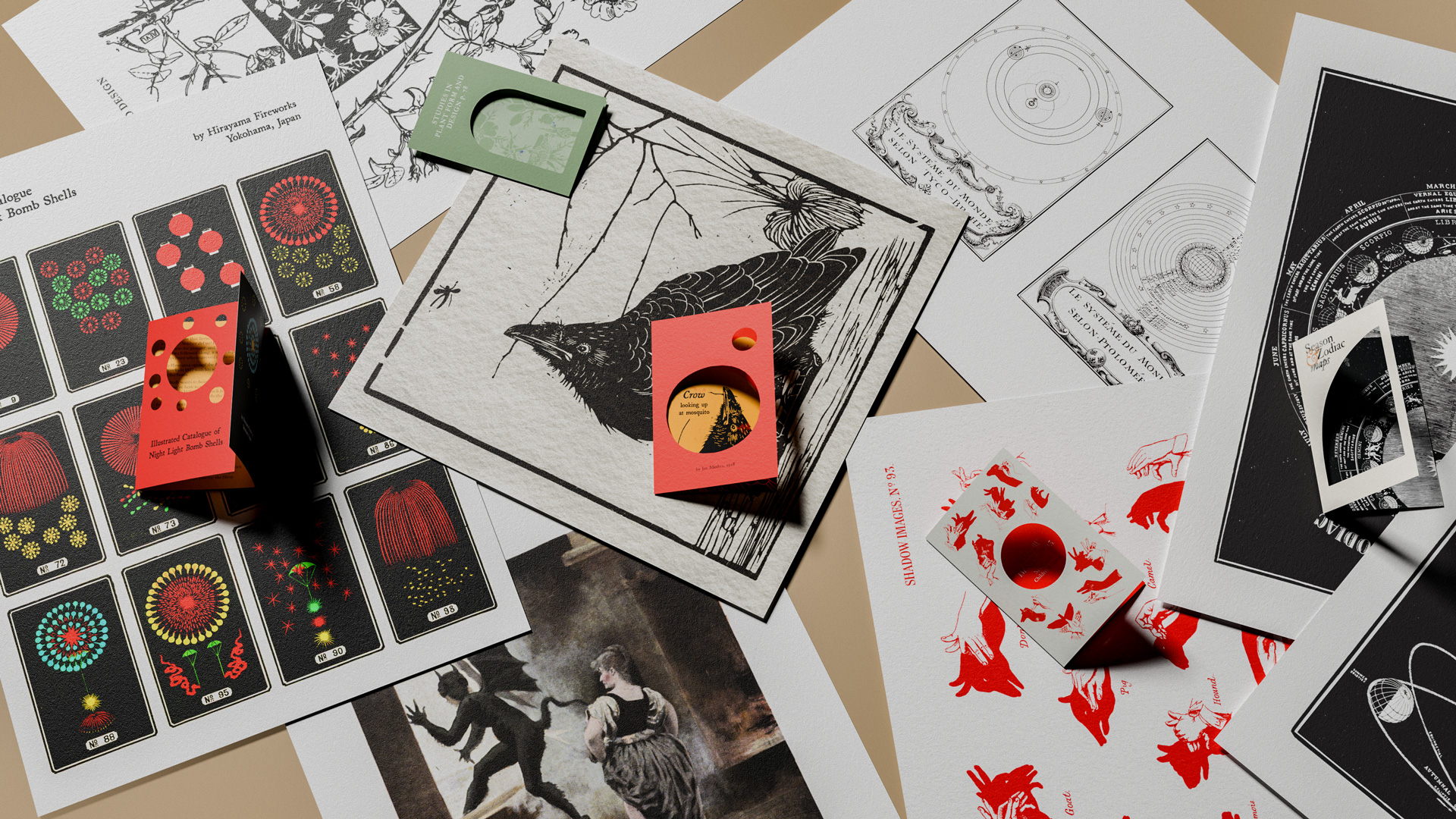Flat lay of various vintage-style illustrated prints including a crow, celestial maps, red animal silhouette shadows, and colorful bomb shell diagrams with small cards displaying text and cut-out circles.
