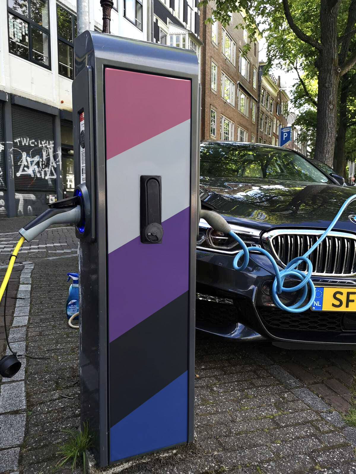 Electric vehicle charging station decorated with a gradient pride flag, charging a black BMW car with blue cable on a city street.