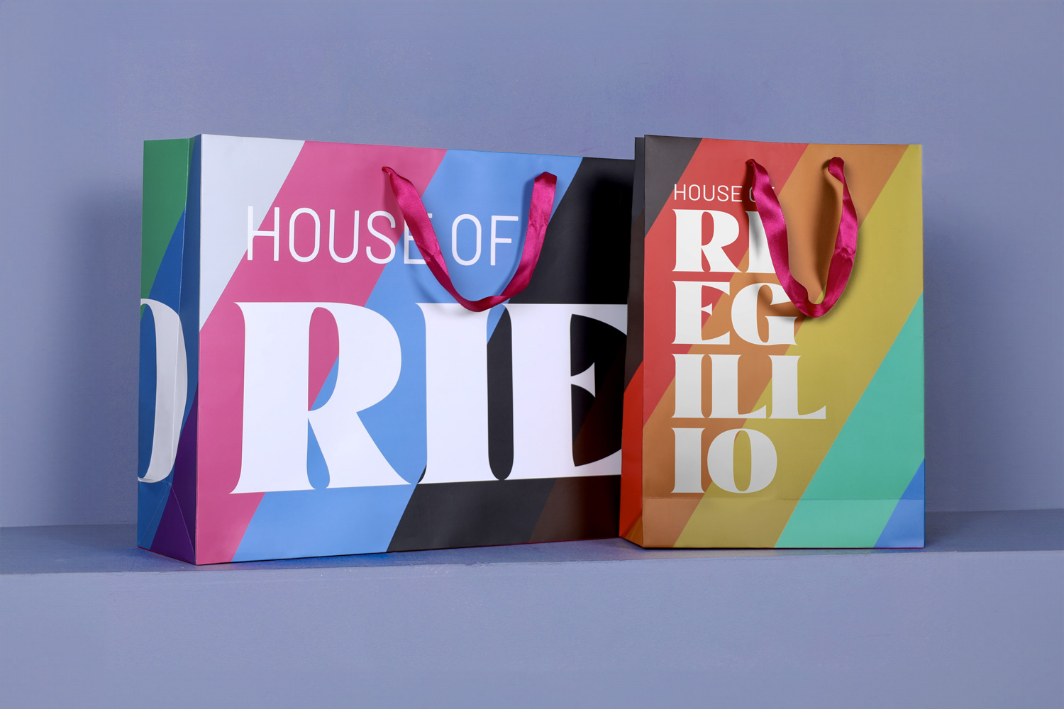 Two colorful shopping bags side by side with diagonal stripes and magenta handles, displaying the text 'HOUSE OF RE' and 'HOUSE OF REGILLO'.