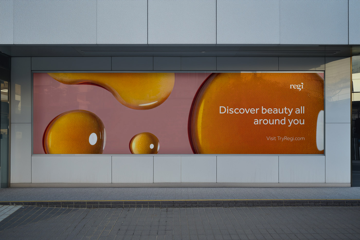 Urban billboard with close-up image of orange droplets and text reading 'Discover beauty all around you' and 'Visit TryRegi.com'.