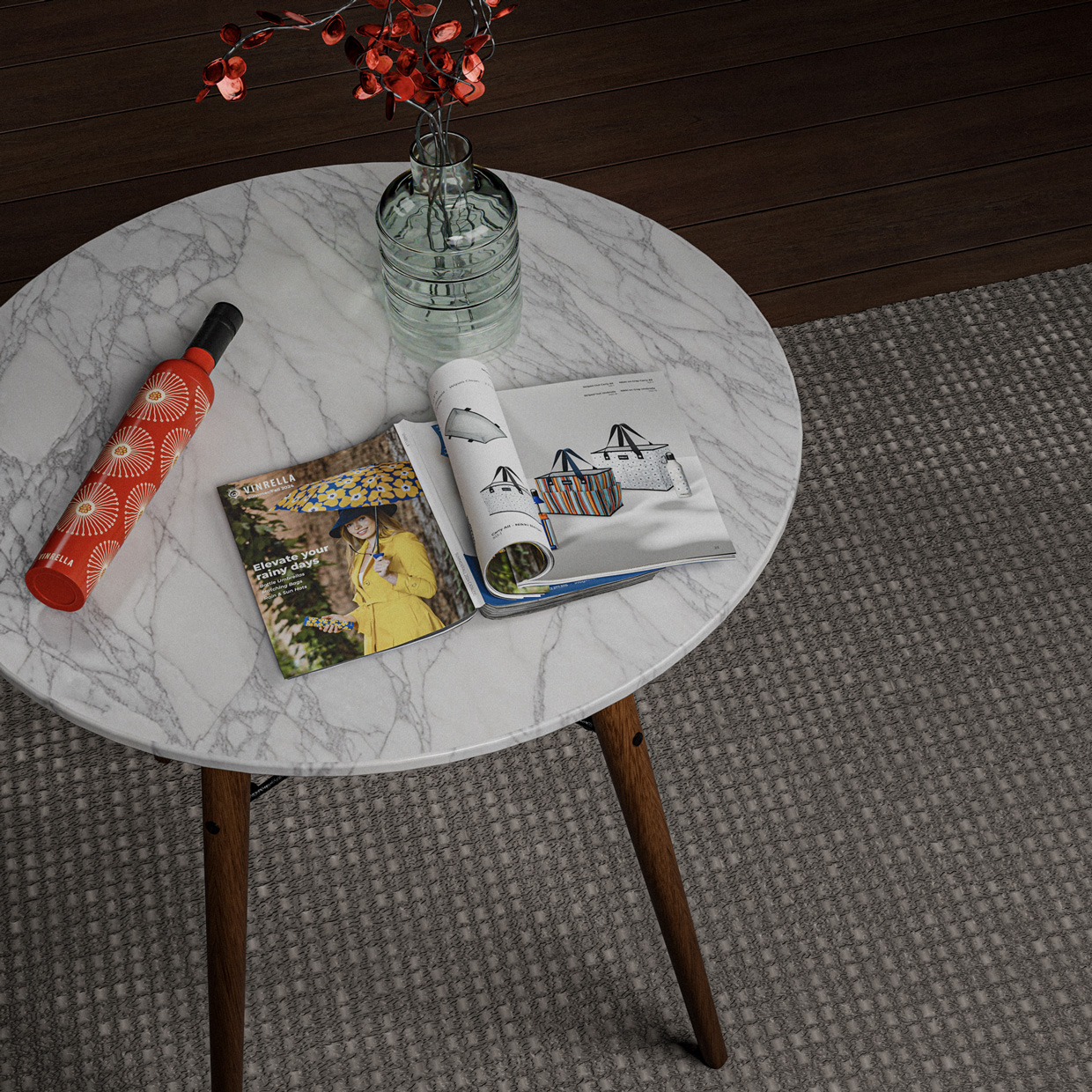 Marble-top round table with wooden legs holding a red patterned wine bottle, a glass vase with red flowers, and an open catalogue displaying colorful bags and a yellow coat with a blue umbrella.